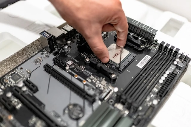 Mężczyzna wkładający nowy procesor firmy AMD do nowej płyty głownej koloru czarnego.